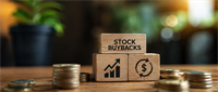 Wooden blocks reading "Stock Buybacks" with chart and dollar icons, surrounded by stacked coins on a table.