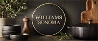 Williams Sonoma circular logo sign on a wall surrounded by kitchenware, bowls, a pepper mill, and cutting board.