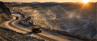 Large haul trucks travel a winding road through an open-pit mine at sunrise or sunset.