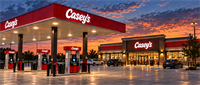 Casey's convenience store and fuel station with gas pumps and parked cars at dusk, illuminated Casey's signage visible.