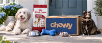 A dog and cat sit beside a Chewy delivery box, Royal Canin dog food bag, and pet supplies on a porch.