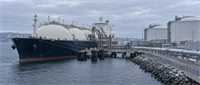 LNG tanker with rounded storage domes docked at a coastal terminal with large storage tanks and pipelines.
