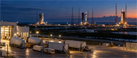 Aerial twilight view of multiple rockets on launch pads at Kennedy Space Center, with support towers and ground vehicles.