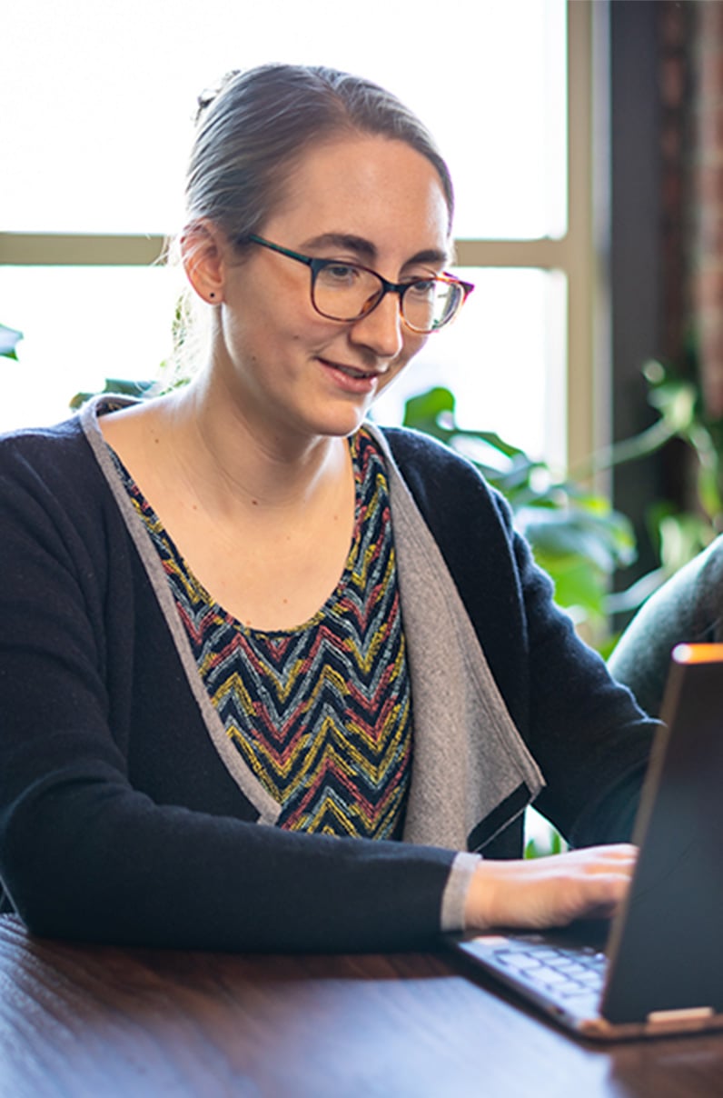 Employee working on laptop in front of office window by plants