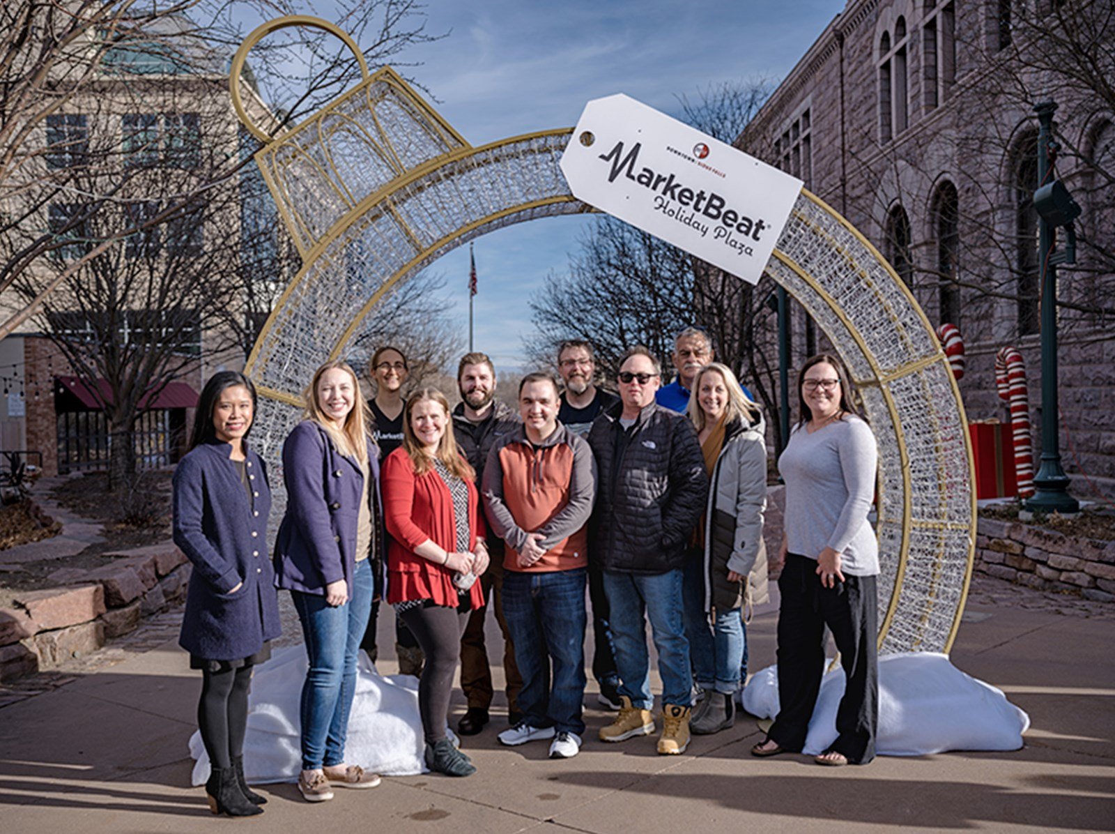 MarketBeat employees in front of a ornament-shaped arc at the Holiday Plaza in Sioux Falls